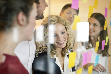 Business people discussing in front of glass screen with sticky notes - PESF00577