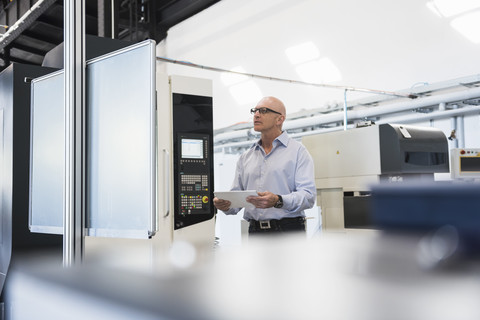 Mann mit Tablet an einer Maschine in einer Fabrikhalle, lizenzfreies Stockfoto