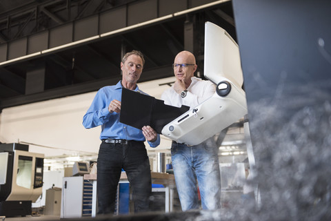 Zwei Männer betrachten ein Klemmbrett in einer Fabrik, lizenzfreies Stockfoto