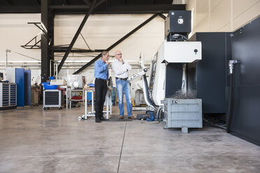 Two men talking at machine on factory shop floor - DIGF02455