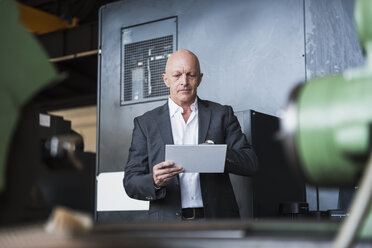Mann mit Tablet an einer Maschine in einer Fabrikhalle - DIGF02465