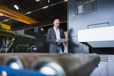 Mann mit Tablet an einer Maschine in einer Fabrikhalle - DIGF02468