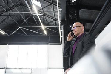 Businessman on cell phone on factory shop floor - DIGF02481