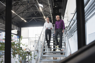 Zwei Geschäftsleute mit Tablet gehen die Treppe in einer Fabrikhalle hinunter - DIGF02483