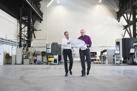 Two businessmen with plan walking in factory shop floor stock photo