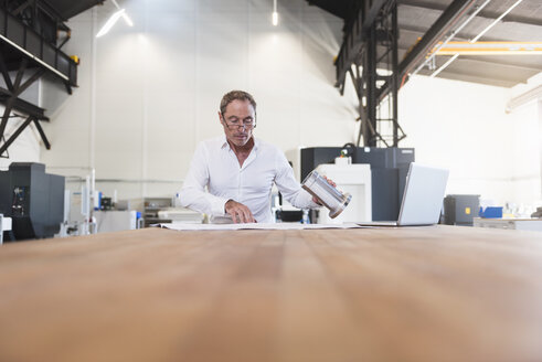 Mann mit Plan, Produkt und Laptop auf einem Tisch in einer Fabrik - DIGF02488