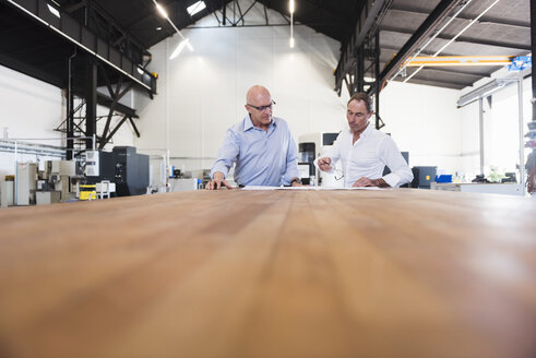 Zwei Geschäftsleute betrachten einen Plan auf einem Tisch in einer Fabrik - DIGF02490