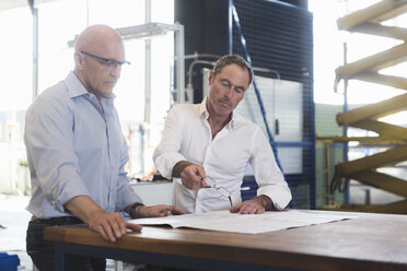 Two businessmen looking at plan on table in factory - DIGF02494