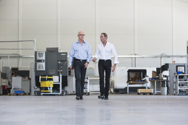 Two businessmen walking and talking in factory shop floor - DIGF02499