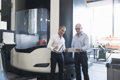 Zwei Männer betrachten ein Tablet und ein Produkt in einer Fabrik - DIGF02502