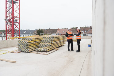 Zwei Männer mit Sicherheitswesten unterhalten sich auf einer Baustelle - DIGF02508