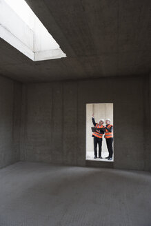 Two men wearing safety vests talking in building under construction - DIGF02511