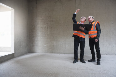 Two men wearing safety vests talking in building under construction - DIGF02512