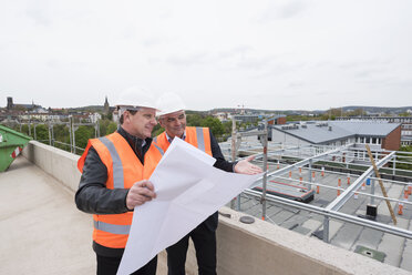 Zwei Männer mit Plan und Sicherheitswesten im Gespräch auf einer Baustelle - DIGF02515