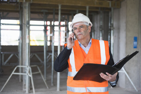 Mann am Telefon mit Sicherheitsweste in einem im Bau befindlichen Gebäude - DIGF02523