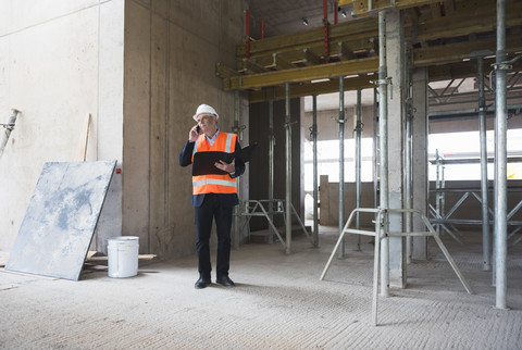 Mann am Telefon mit Sicherheitsweste in einem im Bau befindlichen Gebäude, lizenzfreies Stockfoto