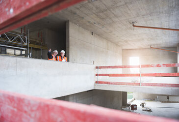 Two men wearing safety vests talking in building under construction - DIGF02526