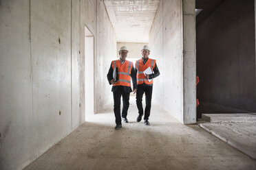 Two men wearing safety walking in building under construction - DIGF02527