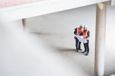 Two men with plan wearing safety vests talking in building under construction - DIGF02529