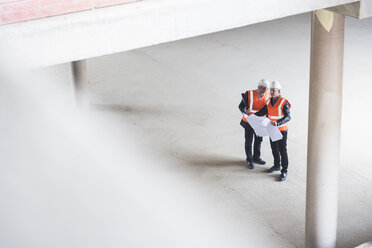 Zwei Männer mit Plan, die Sicherheitswesten tragen, unterhalten sich in einem im Bau befindlichen Gebäude - DIGF02529