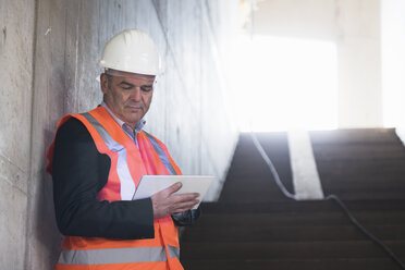 Mann mit Tablet und Sicherheitsweste in einem im Bau befindlichen Gebäude - DIGF02533