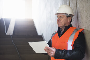 Man with tablet wearing safety vest in building under construction - DIGF02534