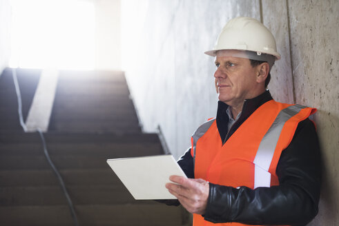 Mann mit Tablet und Sicherheitsweste in einem im Bau befindlichen Gebäude - DIGF02534