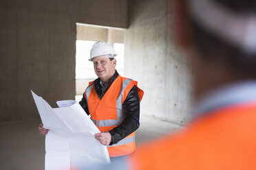 Mann mit Plan und Sicherheitsweste in einem im Bau befindlichen Gebäude - DIGF02540