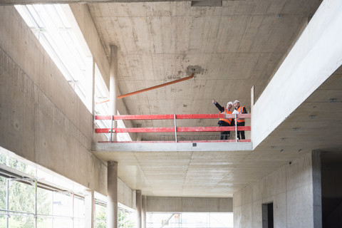 Zwei Männer mit Sicherheitswesten unterhalten sich in einem im Bau befindlichen Gebäude, lizenzfreies Stockfoto