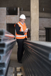 Man with cell phone wearing safety vest in building under construction - DIGF02547