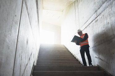 Mann mit Dokumenten und Sicherheitsweste in einem im Bau befindlichen Gebäude - DIGF02548