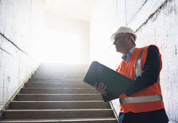 Mann mit Dokumenten und Sicherheitsweste in einem im Bau befindlichen Gebäude - DIGF02549