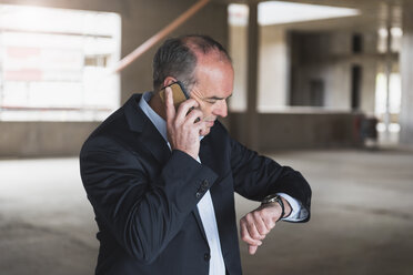 Geschäftsmann mit Handy in einem im Bau befindlichen Gebäude, der die Zeit überprüft - DIGF02552