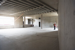 Man wearing safety vest looking around in building under construction - DIGF02556