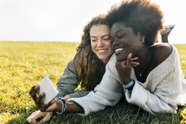 Two best friends lying in grass with cell phone - MGOF03342