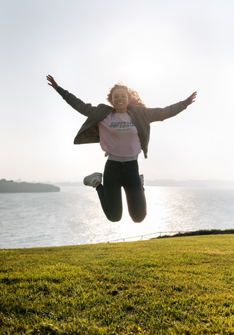 Junges Mädchen springt an der Küste, lizenzfreies Stockfoto
