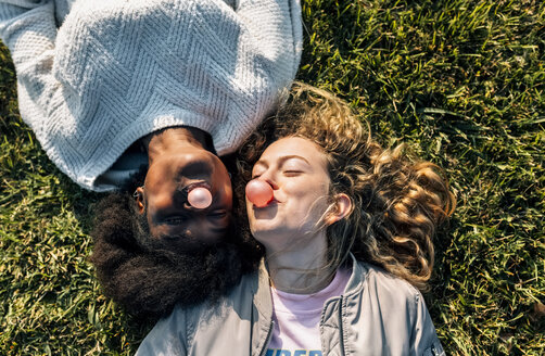 Zwei beste Freunde machen im Gras liegend eine Kaugummiblase - MGOF03358