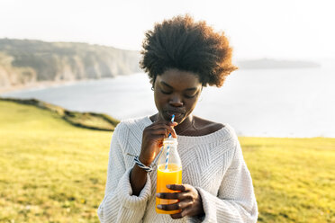 Young woman drinking orange juice at the coast - MGOF03359