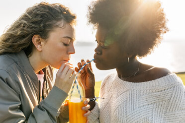 Two best friends drinking orange juice outdoors - MGOF03360