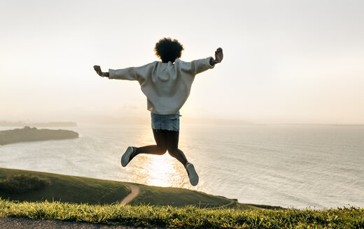 Junge Frau springt bei Sonnenuntergang an der Küste - MGOF03387