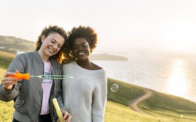 Zwei beste Freunde machen Seifenblasen im Freien bei Sonnenuntergang - MGOF03389