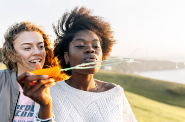 Two best friends making soap bubbles outdoors at sunset - MGOF03392