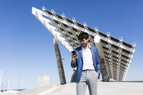 Junger Geschäftsmann schaut im Freien auf sein Smartphone, lizenzfreies Stockfoto