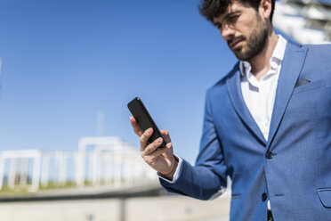 Junger Geschäftsmann schaut im Freien auf sein Smartphone - GIOF02568