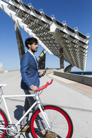 Junger Geschäftsmann mit Fixie-Bike und Smartphone im Freien, lizenzfreies Stockfoto