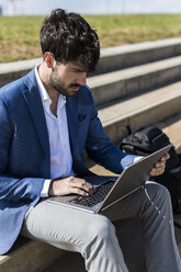 Junger Geschäftsmann sitzt auf einer Treppe und benutzt einen Laptop - GIOF02581