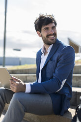 Smiling young businessman sitting on stairs with laptop turning round - GIOF02582