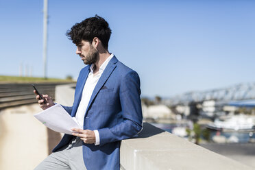 Young businessman with smartphone and documents outdoors - GIOF02584