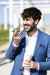 Glücklicher junger Geschäftsmann mit Smartphone und Kaffee zum Mitnehmen im Freien - GIOF02593