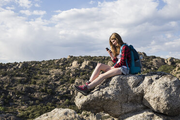 Spanien, Madrid, junge Frau ruht sich auf einem Felsen aus und telefoniert während einer Wanderung - ABZF01999
